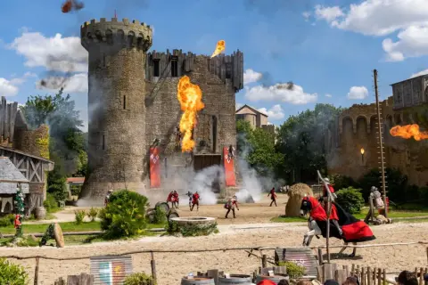 Spectacle de feu et de chevaliers devant le **château du Puy du Fou**. Des flammes jaillissent du donjon, des combattants s'affrontent.