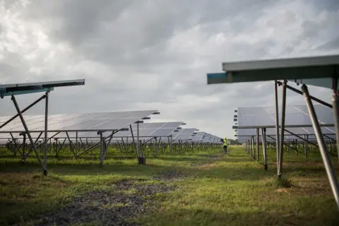 Un campo de paneles solares bajo un cielo nublado. A pesar de la falta de sol directo, las placas solares cargan energía, demostrando su eficiencia.