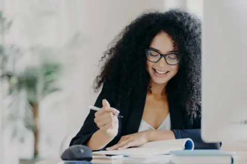 Mujer sonríe mientras escribe, pensando en como empezar una carta de motivación.