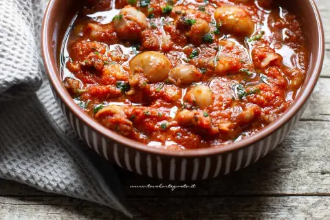 Seppie in padella, succulente e profumate, servite in una ciotola marrone con un contorno di tovagliolo grigio.