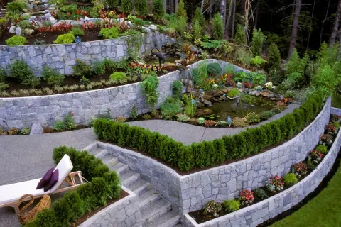 Giardino terrazzato con laghetto e cascata. Muri in pietra che creano livelli, illustrando la differenza tra muro di sostegno e muro di contenimento.