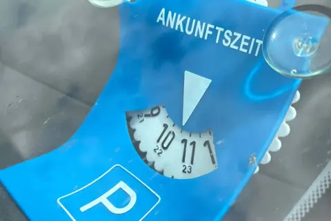 Blaue Parkscheibe mit der Aufschrift "ANKUNFTSZEIT". Die Scheibe ist auf 10:30 Uhr eingestellt, was 15 Minuten Parkzeit bedeutet.