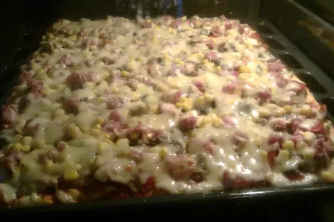 Pyszne ciasto do pizzy z serem, kukurydzą i wędliną, pieczone w piekarniku. Idealne na rodzinny obiad.
