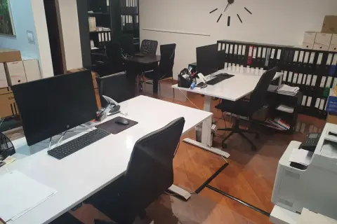 Nowoczesne biuro z biurkami, komputerami, regałami z segregatorami i zegarem na ścianie.