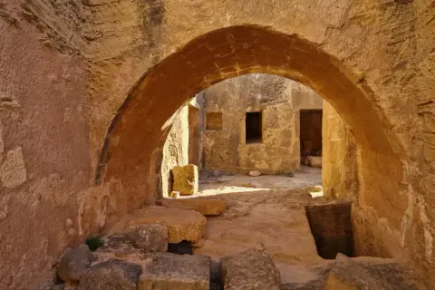 Kamienne łuki i korytarze w grobowcach królewskich Pafos, gdzie słońce rzuca długie cienie na starożytne mury.