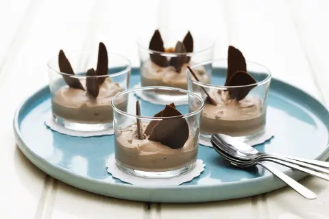 Fyra glas med len choklad dessert, dekorerade med chokladflarn, står på en turkos bricka. En perfekt avslutning på middagen.