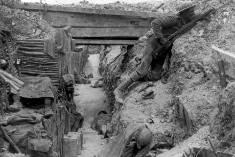 Soldado en posición de combate en las trincheras de la Primera Guerra Mundial. Otros soldados descansan o duermen en el fondo.