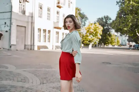 Kobieta w miętowej bluzce i czerwonej spódnicy, zastanawia się, jaka bluzka do czerwonej spódnicy pasuje najlepiej.