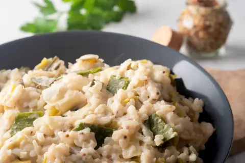 Un crémeux risotto poireaux, parsemé de grains de moutarde, servi dans un bol gris.