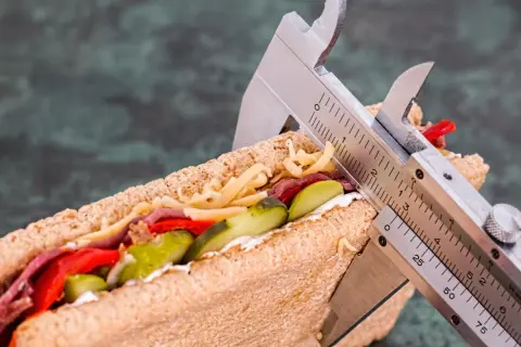 Messung eines Sandwiches mit einem Messschieber, um die Kalorienaufnahme zu kontrollieren. Vielleicht 1500 Kalorien am Tag?