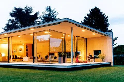 Ein moderner Bungalow mit Glasfronten und einem flachen Dach. Eine Familie entspannt sich auf der Terrasse.