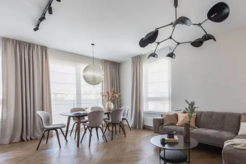 Nowoczesne oświetlenie salonu z jadalnią: designerska lampa nad stołem i reflektory na suficie tworzą przytulną atmosferę.
