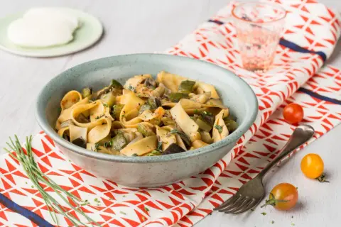 Un plat de pâtes one pot aux légumes d'été, courgettes, aubergines et champignons, garni d'herbes fraîches.