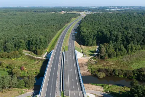 Widok z lotu ptaka na autostradę A1 otoczoną lasem, z mostem nad rzeką.