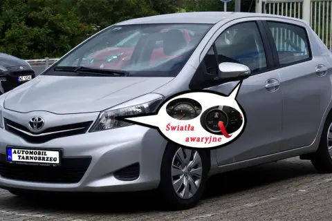 Srebrny Toyota Yaris z zaznaczonymi światłami awaryjnymi. Pod maską kryje się silnik, ale to kontrolki na desce rozdzielczej informują o problemach.