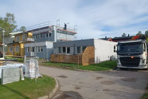 Byggnadsarbetare på ställningar vid hus som ska bygga till. En kranbil står parkerad.