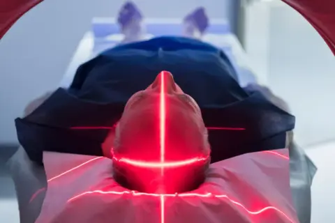 Mann liegt unter roten Laserlinien, die auf seinen Kopf zielen. Dies ist Teil einer neuen Krebstherapie.
