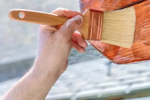 Mano aplicando barniz a madera de pino para exterior. Protegiendo la madera para que dure más.