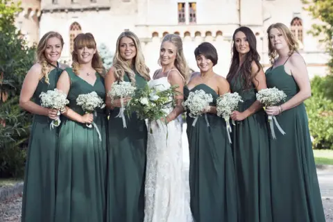 La mariée et ses demoiselles d'honneur, toutes en robes vert d'eau, tiennent des bouquets de fleurs blanches. Un mariage champêtre devant un château.