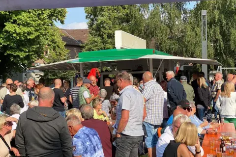 Menschen genießen den feierabendmarkt heute. Viele stehen an einem Imbisswagen, andere sitzen an orangefarbenen Tischen.
