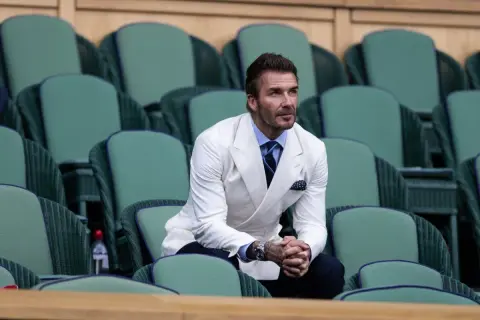 David Beckham in una giacca bianca uomo abbinamento impeccabile, con camicia azzurra e cravatta blu, siede tra le tribune verdi di Wimbledon.