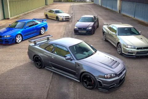 Pięć kultowych Nissanów GT-R R34 w różnych kolorach, stojących na betonowym placu.