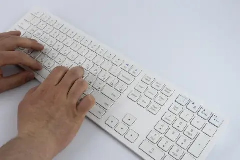 Dłonie piszą na białej klawiaturze. Wskazówki, jak podpisać klawisze na keyboardzie, mogą być pomocne przy nauce.