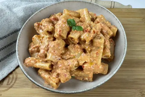 Rigatoni conditi con un cremoso pesto di pomodorini e ricotta, guarniti con basilico fresco.