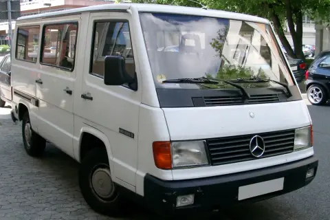 Biały Mercedes MB 100 D, klasyczny van, zaparkowany na ulicy.