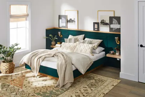 A plush, emerald green headboard with a wooden shelf above offers unique headboard ideas. Artwork and sconces adorn the wall.