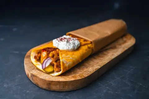 Pyszna shoarma drobiowa z sosem jogurtowym i przyprawami, zawinięta w placek, podana na drewnianej desce.