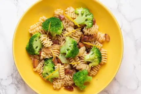 Macarrones con brócoli, trozos de salchicha y ralladura de limón en un plato amarillo.
