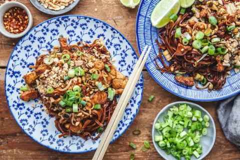 Två tallrikar med läcker pad thai, toppad med jordnötter och salladslök. Ett perfekt pad thai recept för en smakrik måltid.