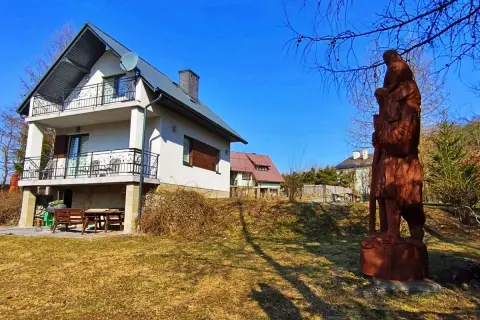 Dom z balkonami i drewniana rzeźba w ogrodzie.