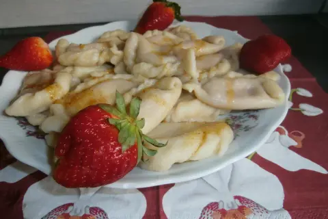 Pyszne pierogi z truskawkami, polane roztopionym masłem, ozdobione świeżymi owocami.