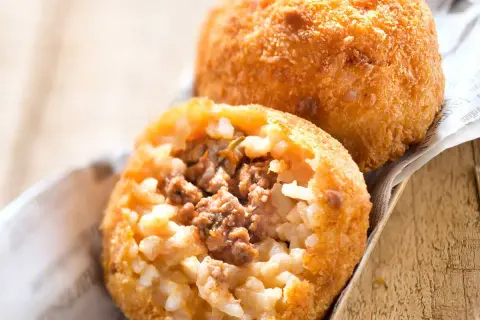 Deux arancini bolognaise dorés et croustillants, l'un ouvert révélant un cœur de riz et de viande savoureux.