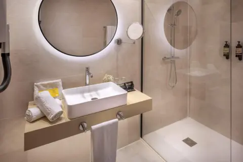 Baño moderno con lavabo sobre encimera y **ducha con suelo de obra**. Toallas blancas y dispensadores de jabón a la vista.