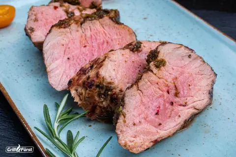 Saftiges Schweinefilet, perfekt gegrillt. Die Kerntemperatur ist entscheidend für dieses zarte Ergebnis. Rosmarin und Tomaten garnieren den Teller.