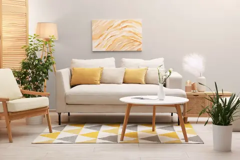 Jasny salon z sofą w kolorze platyny, żółtymi poduszkami i geometrycznym dywanem.