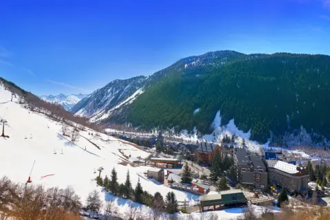 Paisaje nevado del valle de Aran, con pistas de esquí, telesillas y edificios de un pueblo. Ideal para una aventura en autocaravana.