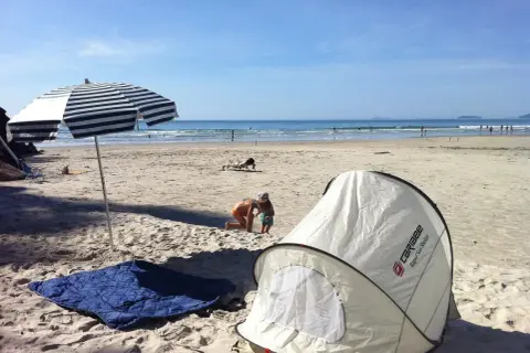 Na plaży rozłożony namiot i koc, idealne miejsce, by sprawdzić, czy można spać na plaży. Dzieci bawią się w piasku, a w tle widać morze.