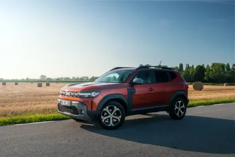 Nowa Dacia Duster w kolorze rudym, zaparkowana na poboczu drogi, z polem słomy w tle.