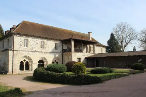 Bâtiment en pierre avec des arches romanes, un balcon et un jardin.