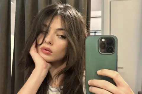 Deva Cassel se toma un selfie con su teléfono, apoyando la barbilla en la mano.