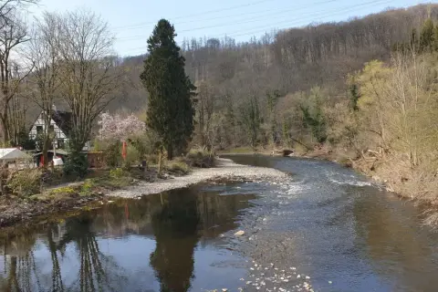 Idyllische Flusslandschaft am Wupperhof Solingen mit Fachwerkhäusern und bewaldeten Hängen.