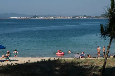 Gente disfruta de un día soleado en las playas de O Grove, con niños jugando en el agua y adultos relajándose en la arena.