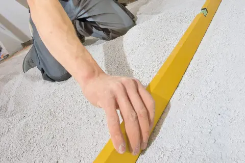 Hand gleicht Schüttung für trockenestrich verlegen mit Richtlatte aus.
