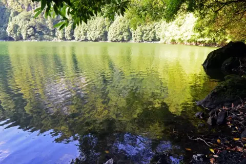 Reflejos verdes y azules en la serena Lagoa do Congro, rodeada de exuberante vegetación y rocas cubiertas de musgo.