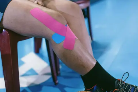 Jambe d'athlète avec un strap quadriceps rose et bleu, prêt pour l'action.