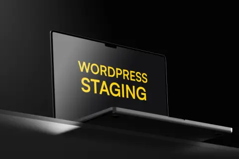 Laptop z napisem "WORDPRESS STAGING" na ekranie, w ciemnym otoczeniu.